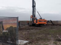 Oranje heimachine slaat de palen van de nieuwbouw huis op bouwplaats in de gornd